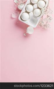 White eggs in white ceramic holder and flowers on pink background, flat lay, copy space