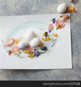 White eggs on paper with flower petals on stone background. Easter eggs with flowers decoration