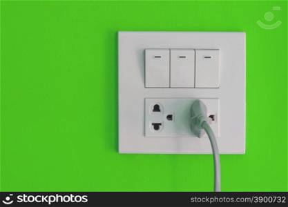 White electric outlet and switch mounted on painted green cement wall