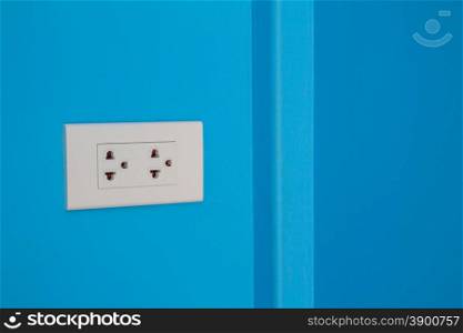 White electric outlet mounted on painted blue cement wall