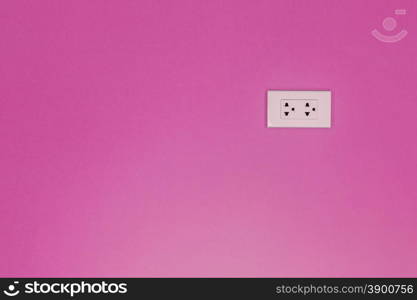 White electric outlet mounted on painted pink cement wall