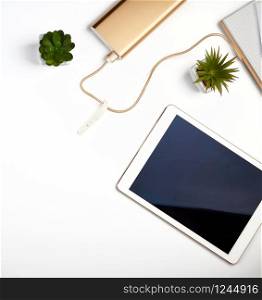 white electronic tablet with a blank black screen, near pots with green plants on a white table, top view, designer workplace