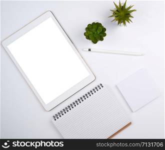 white electronic tablet with a blank screen and a pencil, near pots with green plants on a white table, top view, designer workplace
