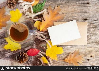 white empty card fall invitation, leaves and coffee on wooden autumn background with copy space on white paper note. Fall leaves autumn background