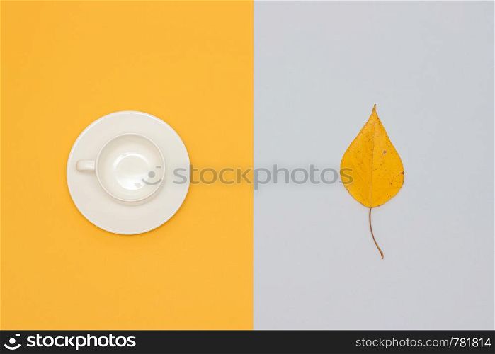White empty cup with saucer and autumn leaf on yellow and gray background. Copy space Flat lay Mock up Template for your design.. White empty cup with saucer and autumn leaf on yellow and gray background. Copy space Flat lay Mock up Template for your design
