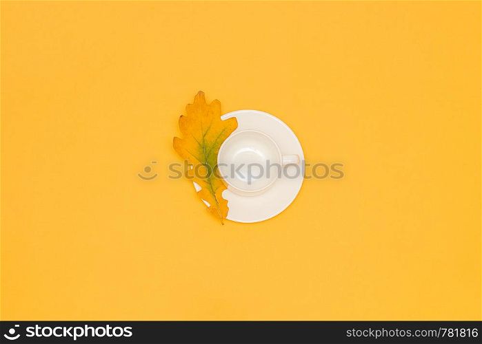 White empty cup with saucer and autumn oak leaf in the center on yellow background. Copy space Flat lay Mock up Template for your design.. White empty cup with saucer and autumn oak leaf in the center on yellow background. Copy space Flat lay Mock up Template for your design