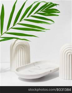 White empty decorative plate on a white background and a palm leaf, a stage for product and cosmetics display