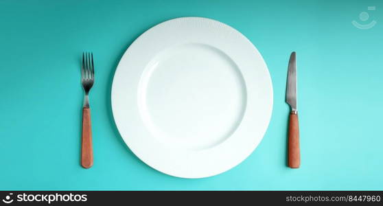 White Empty Plate with Fork and Knife Lay on Blue Table Background. Food Shortage, World Food Crisis Issue. Table Top View 