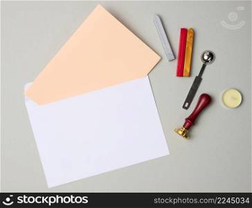 white envelope and items for sealing with wax seal on gray background, flat lay