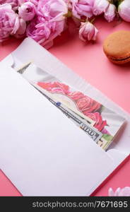  white envelope with cash around roses and macaroons against  pink background. life style concept