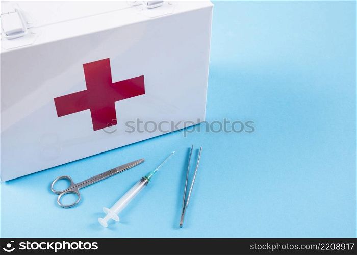 white first aid kit with scissor syringe tweezers blue background