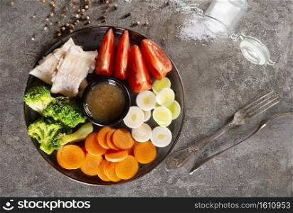 white fish with vegetables, portion of boiled and raw vegetables and fish fillet
