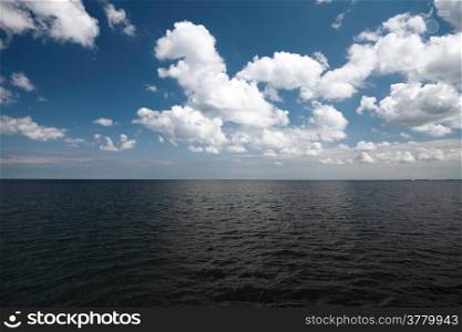 White fluffy clouds blue sky above a dark surface of the sea