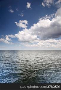 White fluffy clouds blue sky above a dark surface of the sea