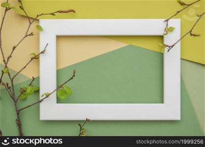 White frame and branches of a tree with young blossoming leaves on geometric green shades paper background. Copy space, mockup for your design. Spring time concept.. White frame and branches of a tree with young blossoming leaves on geometric green shades paper background. Copy space, mockup for your design. Spring time concept