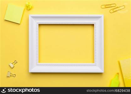 White frame and office accessories on yellow background. Flat lay. Copy space. Top view