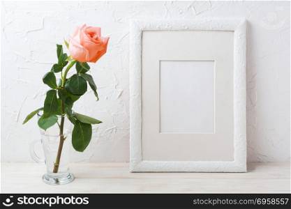 White frame mockup with creamy pink rose in glass vase. Empty frame mock up for presentation artwork.. White frame mockup with creamy pink rose in glass vase