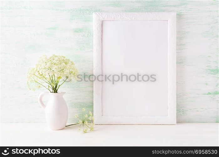 White frame mockup with delicate wild field flowers in pitcher. Empty frame mock up for presentation artwork.. White frame mockup with delicate wild field flowers in pitcher