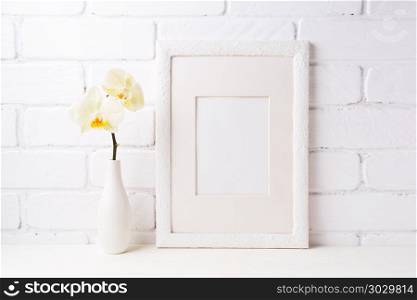 White frame mockup with soft yellow orchid in vase. Empty frame mock up for presentation artwork. Template framing for modern art.. White frame mockup with soft yellow orchid in vase