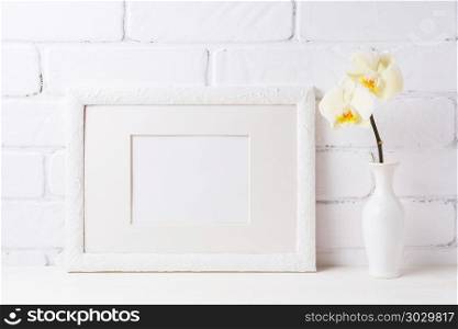 White frame mockup with soft yellow orchid in vase. Empty frame mock up for presentation artwork. Template framing for modern art.. White frame mockup with soft yellow orchid in vase