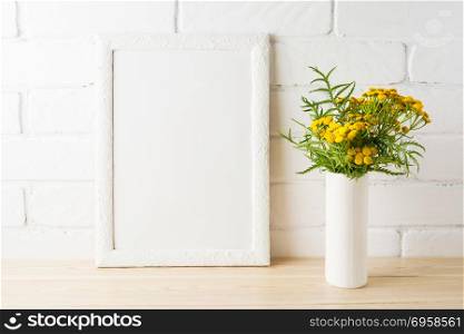 White frame mockup with wild rich golden yellow flowers in vase near painted brick walls. Empty frame mock up for presentation design. Template framing for modern art.. White frame mockup with yellow flowers near painted brick walls