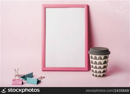 white frame with pink border paper clips coffee disposable cup against pink background