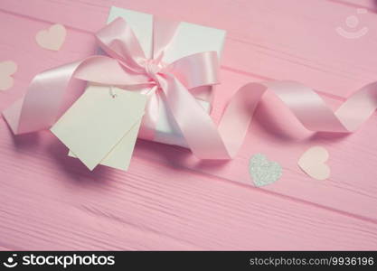 White gift box with a pink satin bow and ribbon on pink wooden background. Wedding mockup tag is included for your text. Can use for Valentines Day, mothers day, birthday.. White gift box with a pink satin bow and ribbon on pink wooden background. Wedding mockup tag is included for your text. Can use for Valentines Day, mothers day, birthday