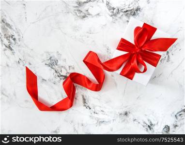 White gift box with red ribbon bow on bright marble background