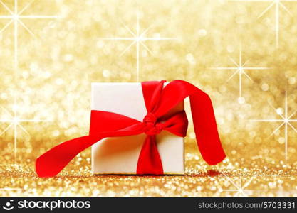 White gift box with red ribbon bow on golden glitter background