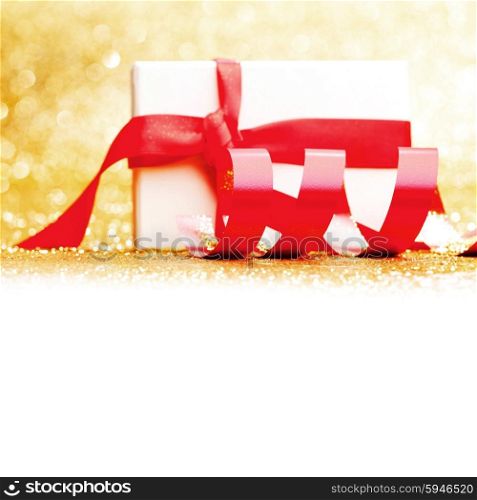 White gift box with red ribbon on golden glitter background