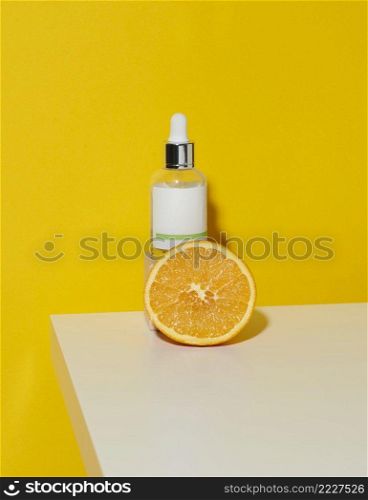 white glass bottle with a pipette and half an orange on a white surface, green background. Citrus extract