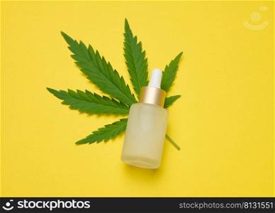 White glass bottle with pipette and green cannabis leaf on yellow background, top view