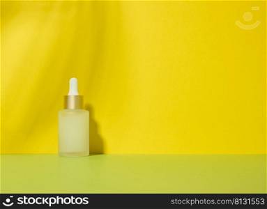 White glass transparent bott≤with aπpette for cosmetics, oils, acids. Yellow background