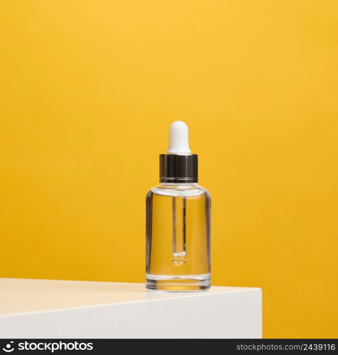 white glass transparent bottle with a pipette for cosmetics, oils, acids on a white table. yellow background