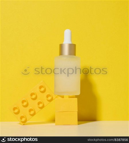 White glass transparent bottle with a pipette for cosmetics, oils, acids on a white table. Yellow background