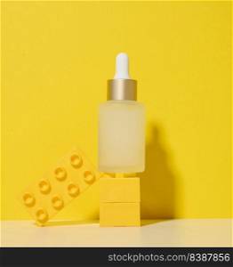 White glass transparent bottle with a pipette for cosmetics, oils, acids on a white table. Yellow background