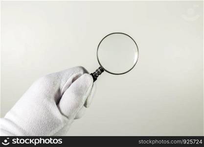 White glove holding magnifier on the gray background.