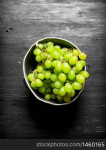 White grapes in the old pot. On a black wooden background.. White grapes in the old pot.