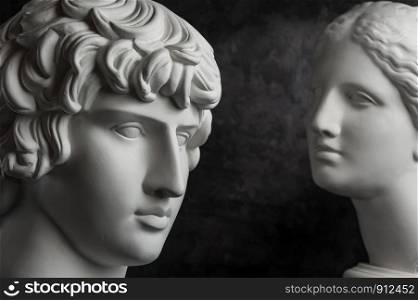 White gypsum copy of ancient statue of Antinous and Venus head for artists on a dark textured background. Plaster sculpture of statue face.. Gypsum copy of ancient statue Antinous and Venus head on dark textured background. Plaster sculpture face.