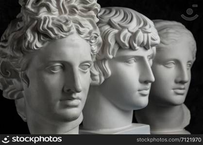 White gypsum copy of ancient statue of Apollo, Antinous and Venus head for artists on a dark textured background. Plaster sculpture of statue face.. Gypsum copy of ancient statue Apollo, Antinous and Venus head on dark textured background. Plaster sculpture face.
