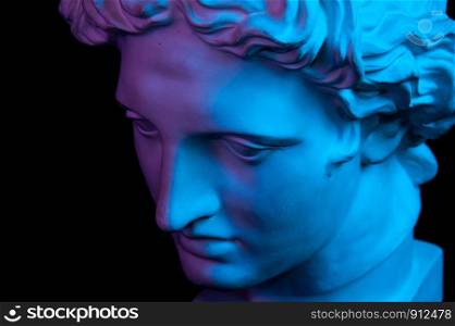 White gypsum copy of ancient statue of Apollo God of Sun head for artists isolated on a black background. Plaster sculpture of man face. Toned blue and purple.. Gypsum copy of ancient statue Apollo head isolated on black background. Plaster sculpture man face.