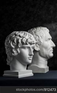 White gypsum copy of ancient statue of Guy Julius Caesar Octavian Augustus and Antinous head for artists on a dark textured background. Plaster sculpture of mans face.. Gypsum copy of ancient statue Augustus and Antinous head on dark textured background. Plaster sculpture mans face.