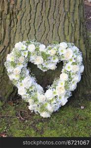 White heart shaped sympathy floral arrangement near a tree