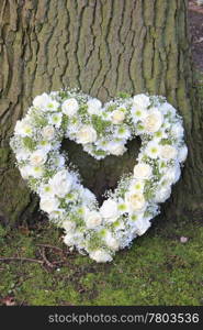 White heart shaped sympathy floral arrangement near a tree