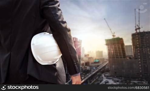 White helmet of engineer architect holding by businessman in suit and building construction site background