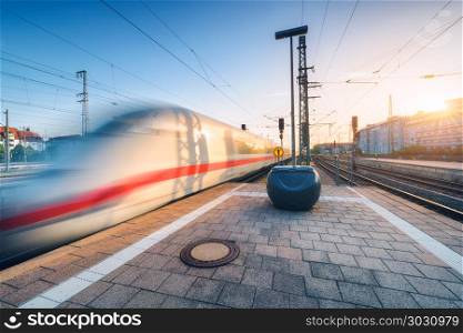 White high speed train in motion on the railway station at sunset. Germany. Blurred modern intercity train on the railway platform. Industry. Passenger train on railroad. Railway travel in Europe. White blurred high speed train on the railway station