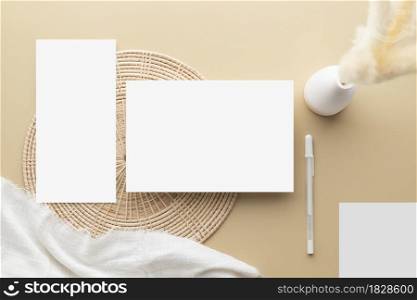 White invitation card, Blank Paper mockup on a beige background, reeds grass in a vase, white blanket, Rattan basket, Flat lay, top view, copy space