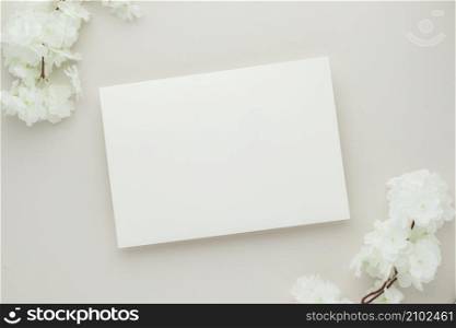 White invitation card mockup with a white flower on beige background, Minimal beige workplace composition, flat lay, mockup