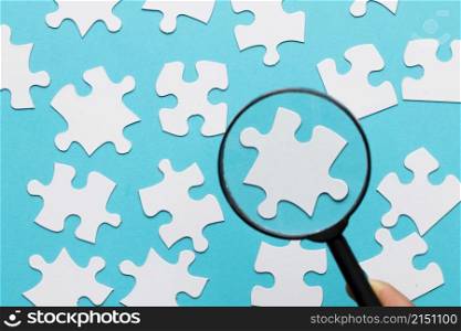 white jigsaw piece seen through magnifying glass blue white background