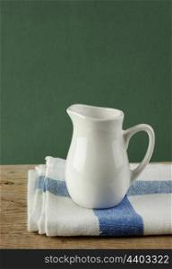 White jug and dishcloth on old wooden table over green background